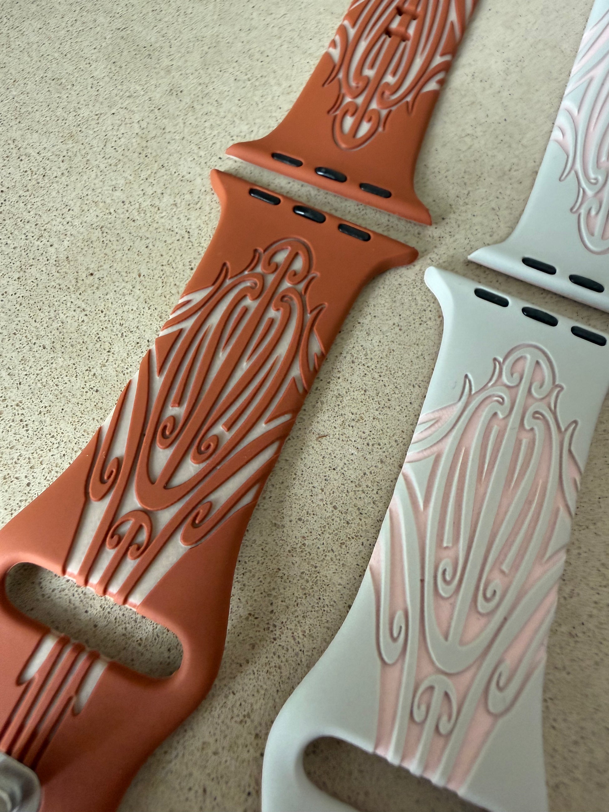 Two watch bands with intricate patterns on a beige surface